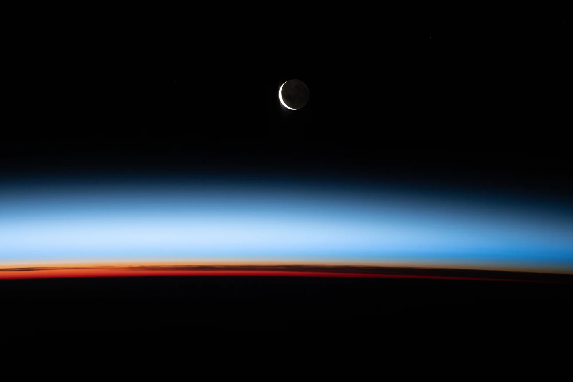 A crescent moon above Earth's night horizon, photographed from the International Space Station